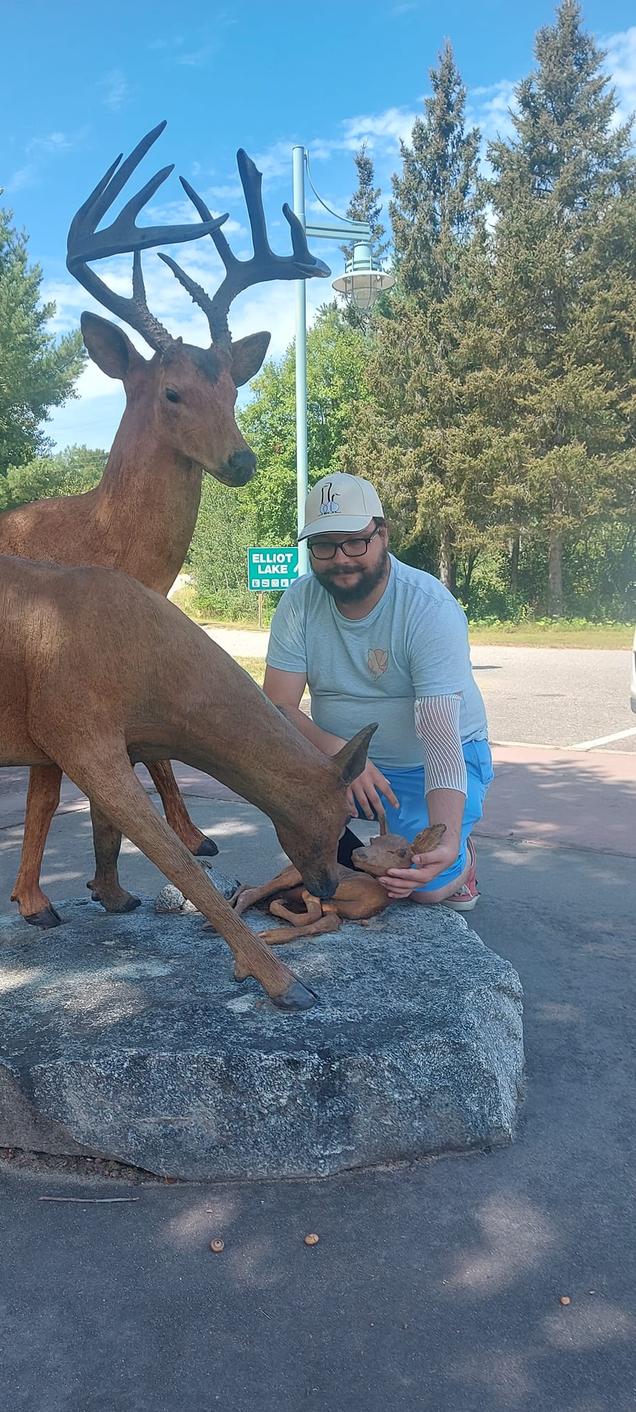 A man short hair and bushy facial hair pretends to hold a baby deer statue